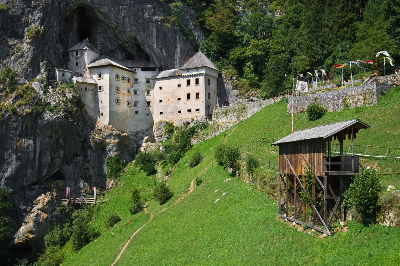 A white castle built into the side of a mountain with green grass and road leading up to it